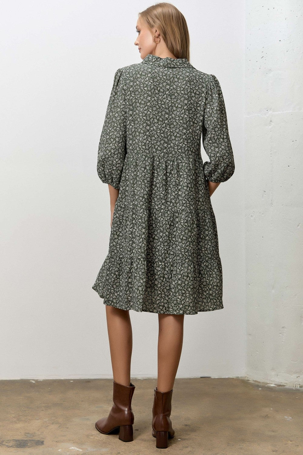 woman wearing a green floral short sleeve dress with a tiered skirt and brown ankle boots, view from the back
