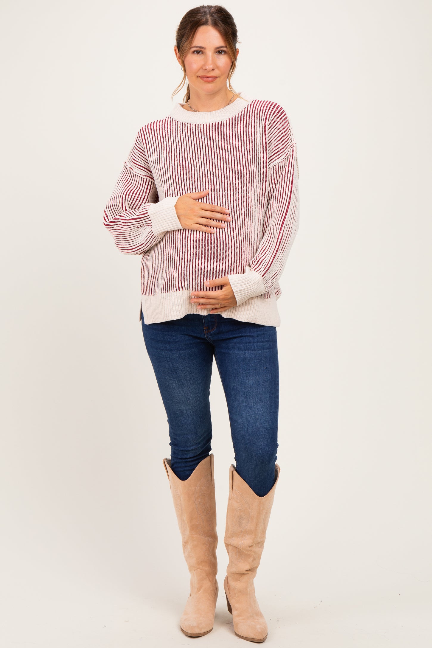 woman wearing a striped red and white maternity sweater and blue jeans, holding her baby bump