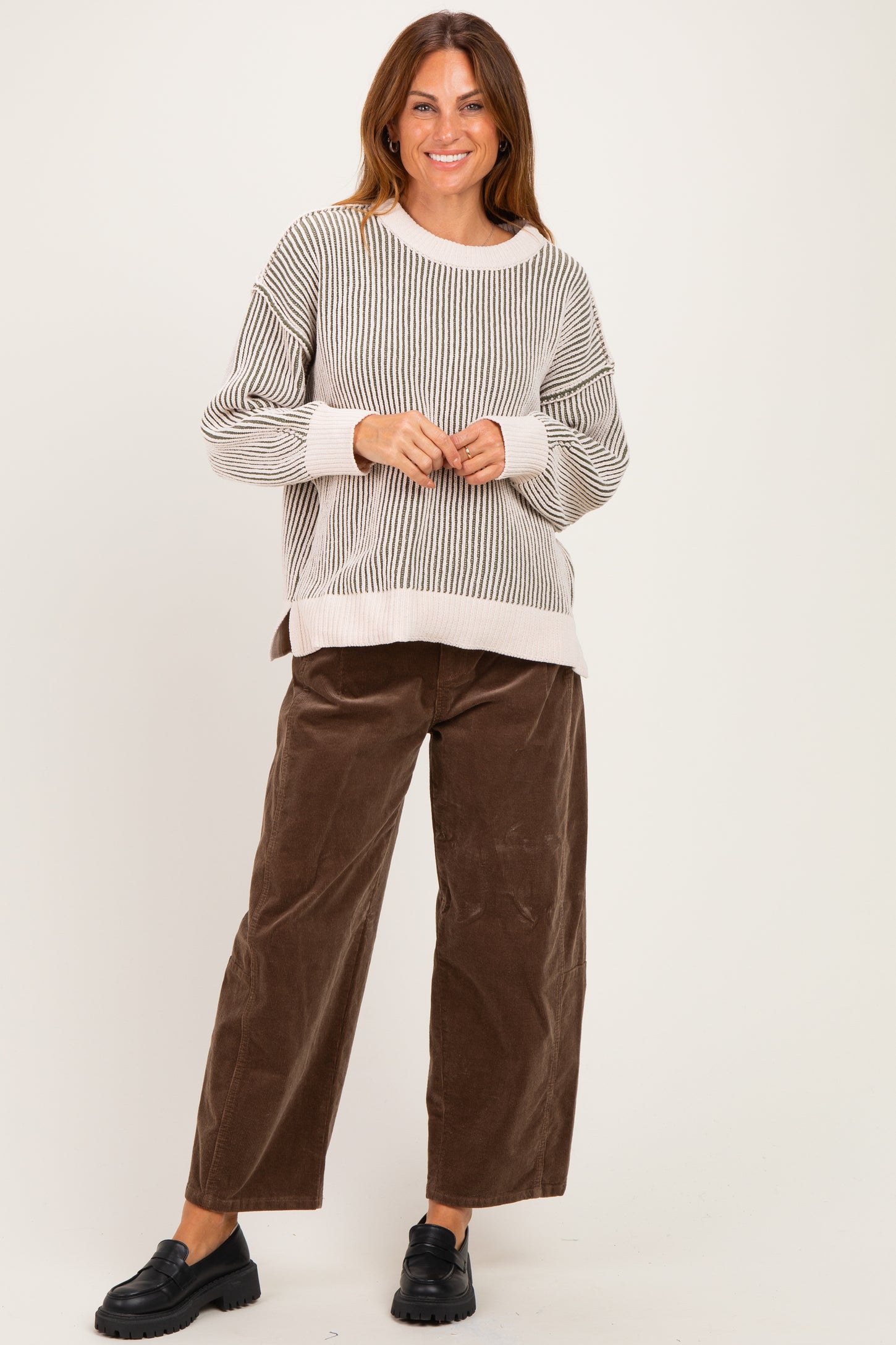 woman wearing a striped oversized sweater and brown wide-leg corduroy pants, standing and smiling