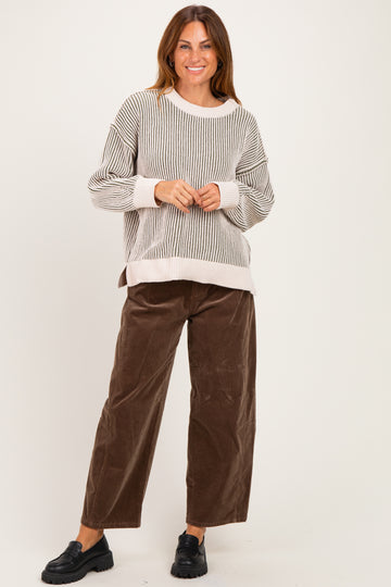 woman wearing a striped oversized sweater and brown wide-leg corduroy pants, standing and smiling