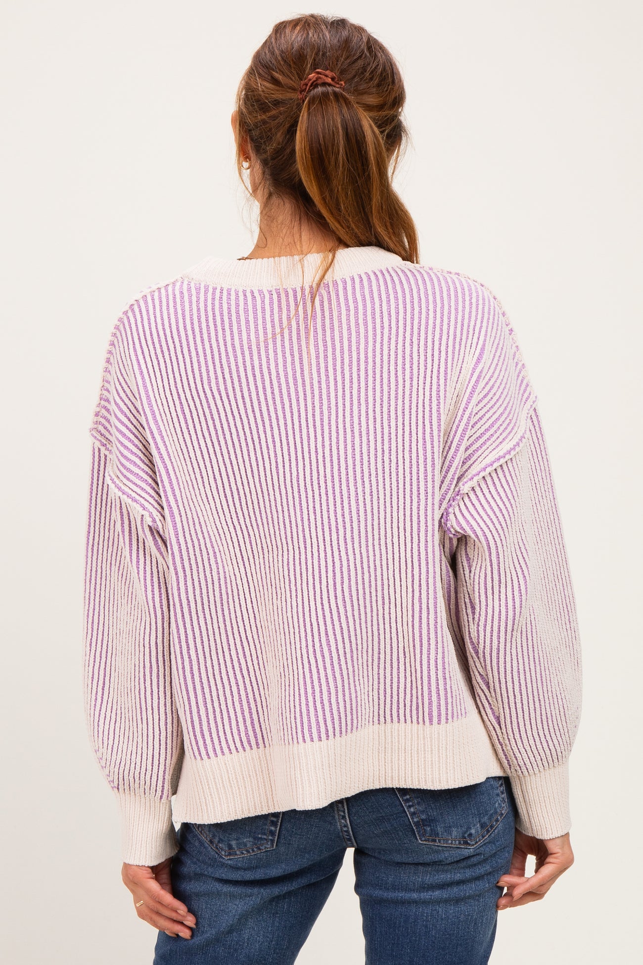 woman wearing a back view of a light beige and lilac striped oversized sweater with balloon sleeves and blue jeans