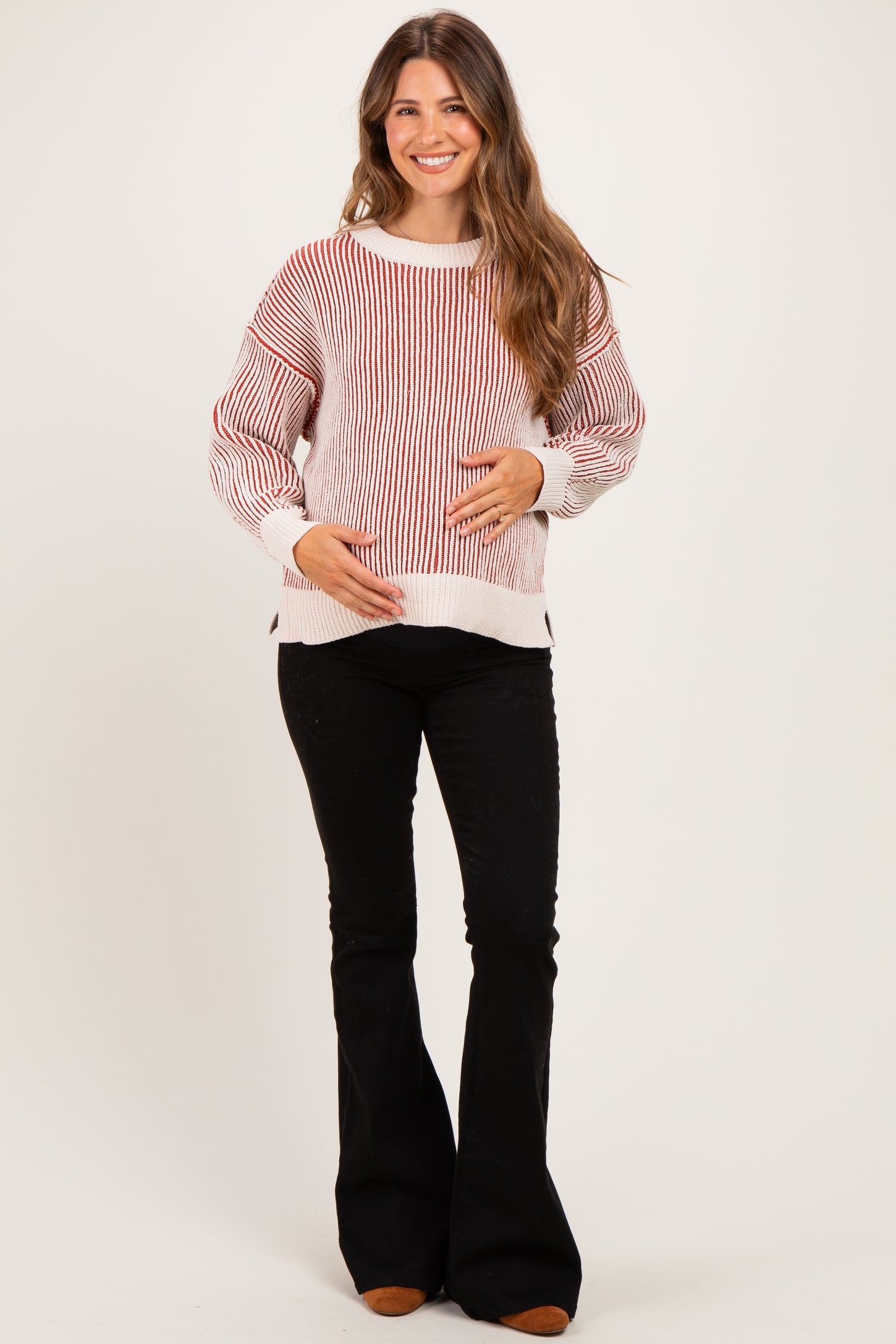 woman wearing a red and white striped maternity sweater and holding her baby bump, paired with black flared pants