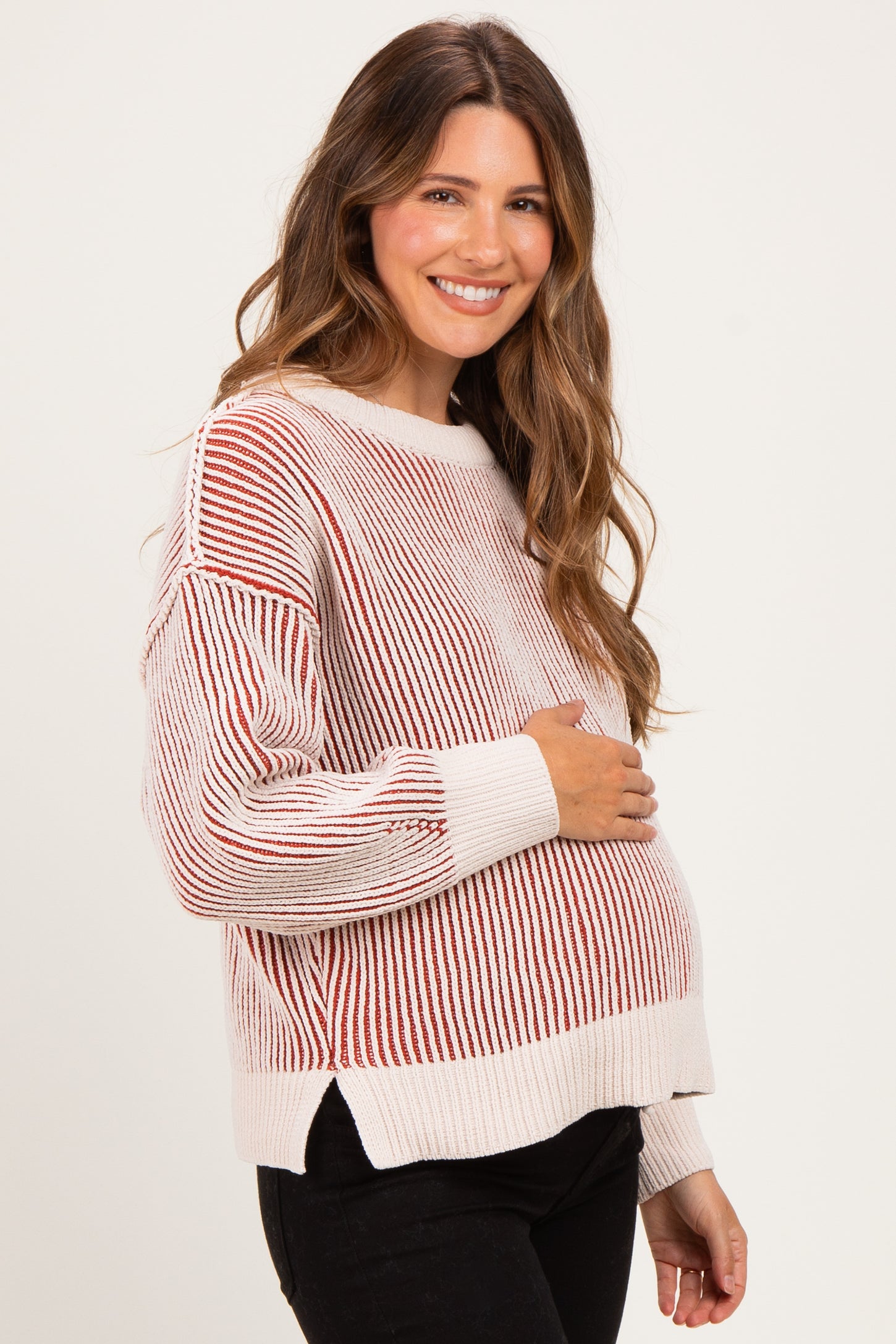 woman wearing a striped maternity sweater in cream and rust, holding her baby bump