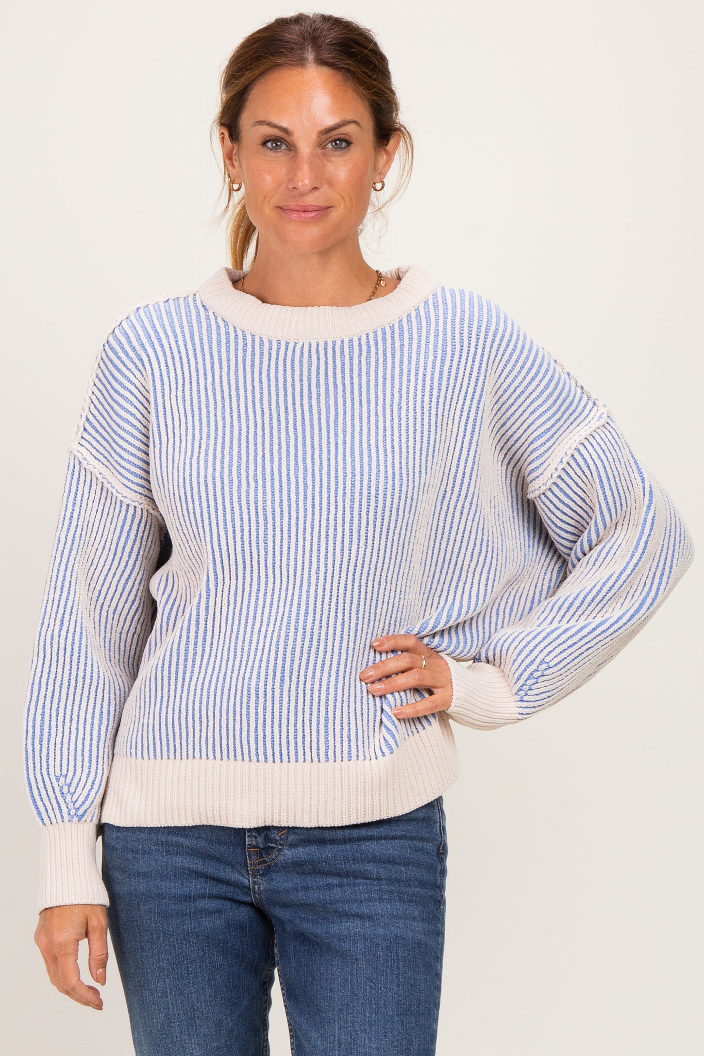 woman wearing a striped light blue and beige oversized sweater with balloon sleeves and casual blue jeans