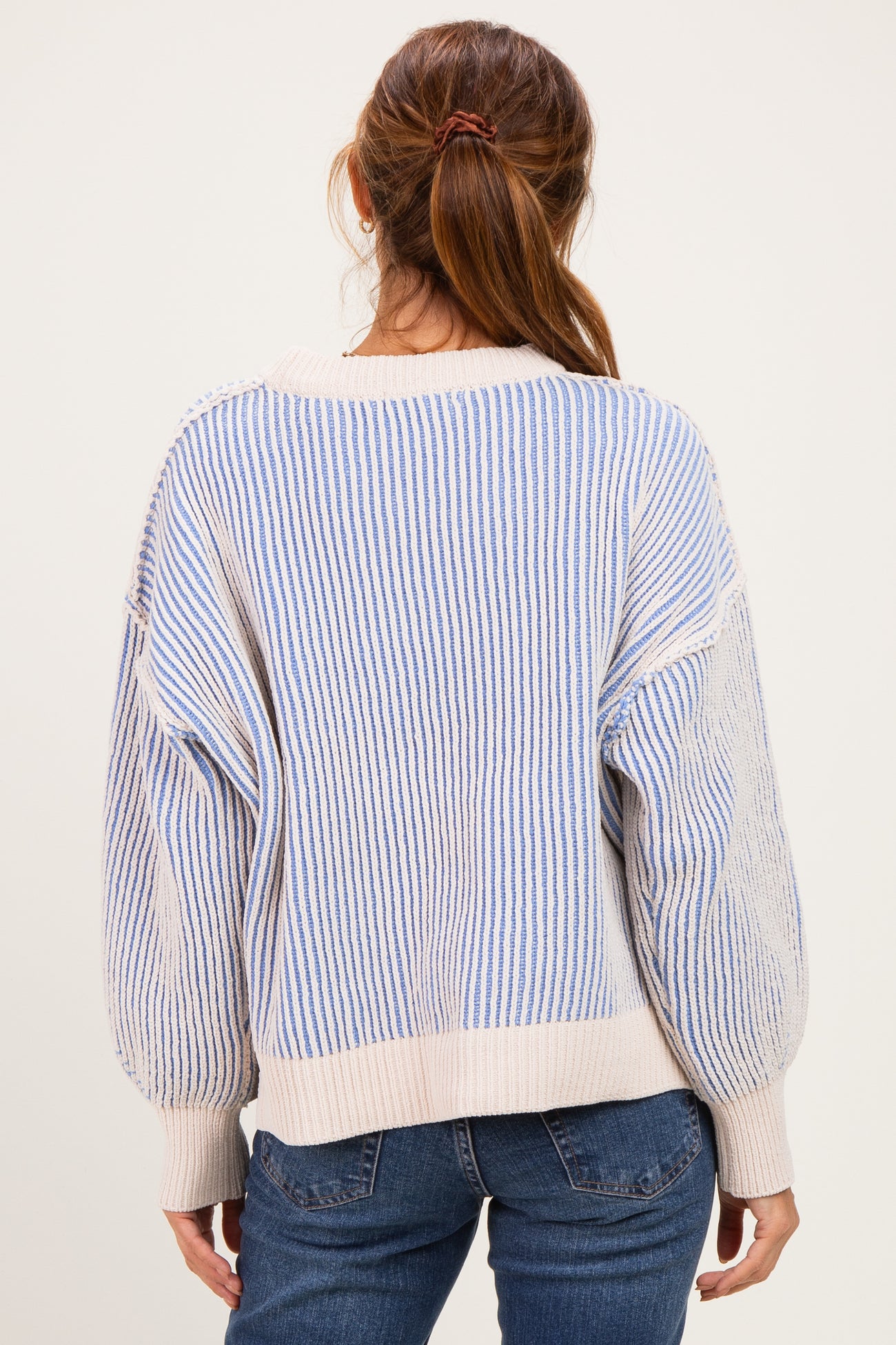 woman wearing a cream and blue striped oversized sweater paired with blue jeans, seen from the back