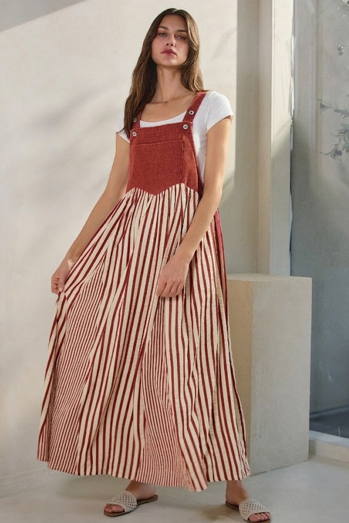 woman wearing a rust-colored striped maxi dress with a white t-shirt underneath and holding the skirt lightly