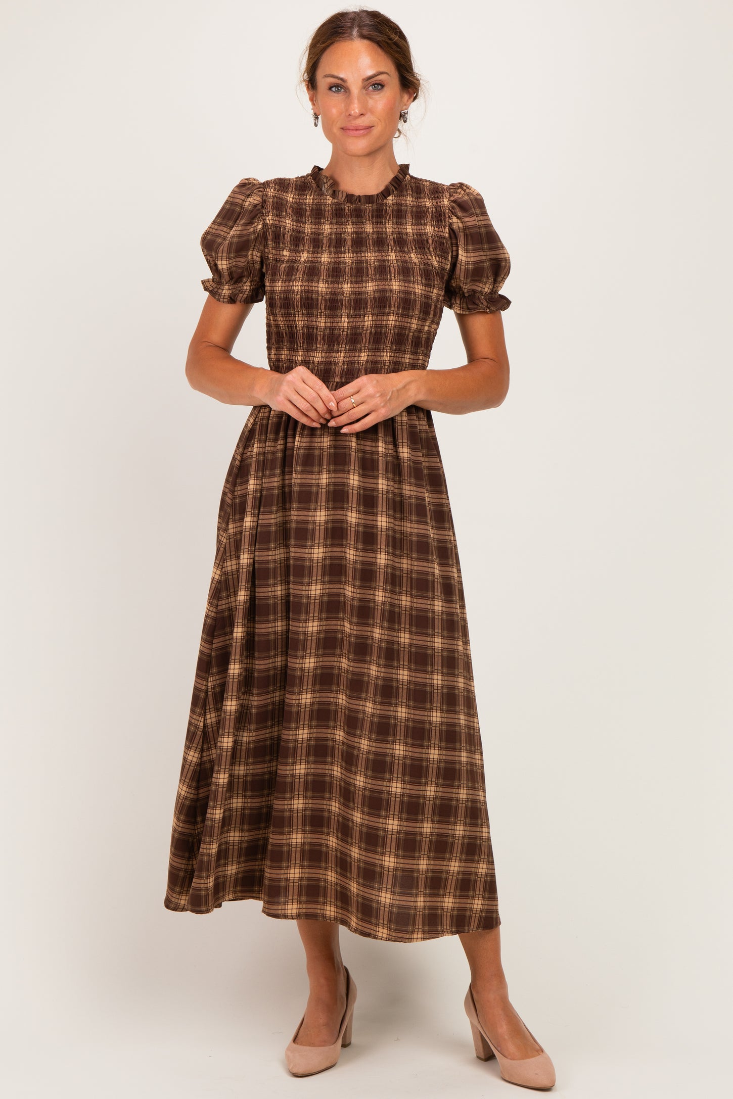 woman wearing a brown and tan plaid midi dress with puff sleeves and a cinched waist, standing in a neutral background