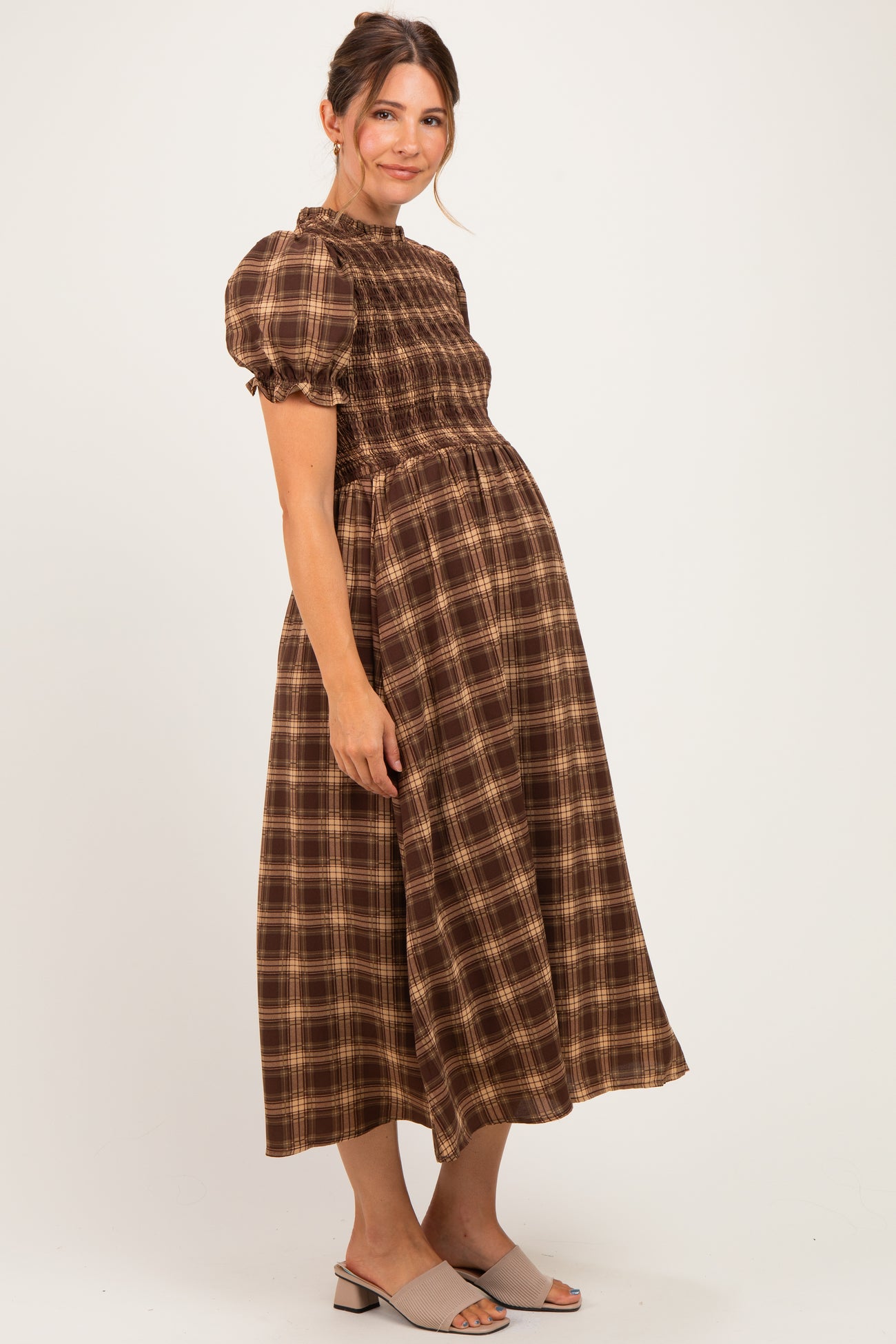 woman wearing a brown plaid maternity dress with puff sleeves and a smocked bodice, highlighting her baby bump