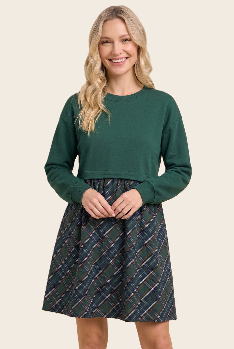 woman wearing a green long sleeve top with a tartan print skirt dress, smiling at the camera