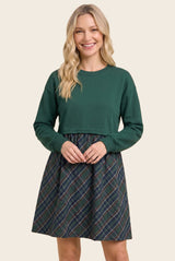 woman wearing a green long sleeve top with a tartan print skirt dress, smiling at the camera