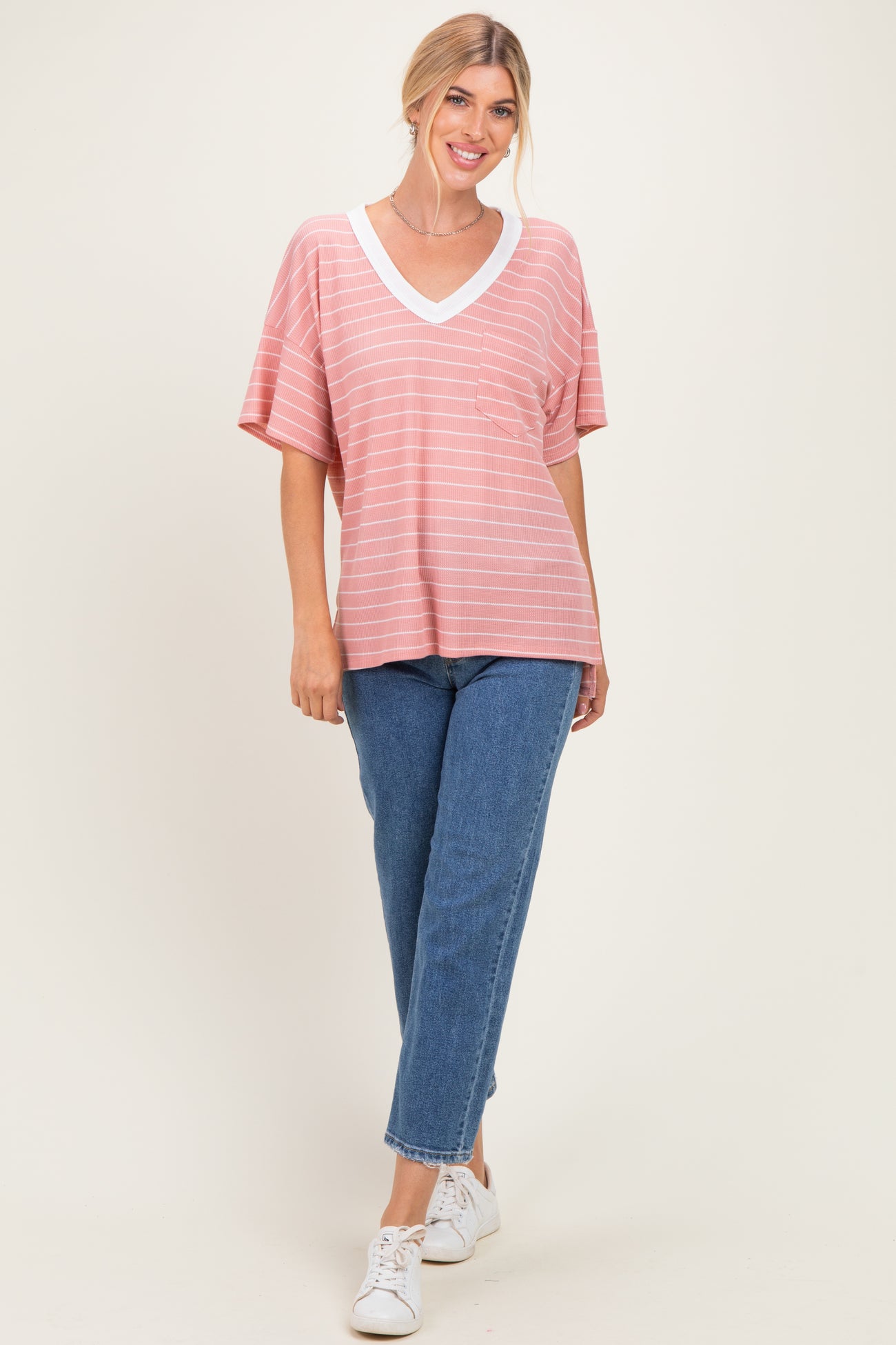woman wearing a coral striped v-neck oversized t-shirt with a pocket and light blue high-waisted jeans