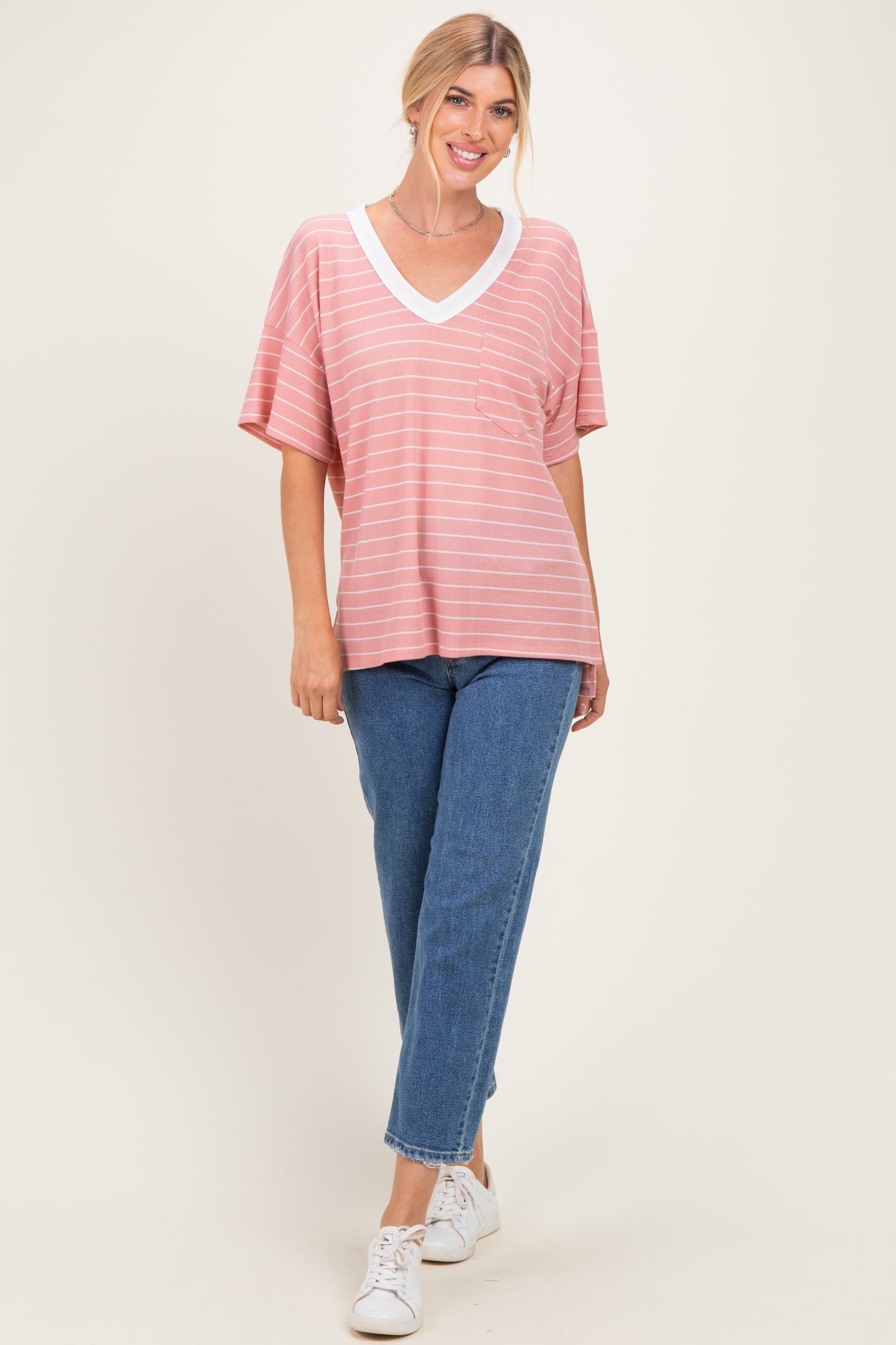 woman wearing a coral striped v-neck oversized t-shirt with a pocket and light blue high-waisted jeans