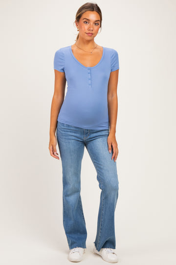 woman wearing a light blue maternity top with short sleeves and a scoop neckline, paired with flare jeans and showing her baby bump