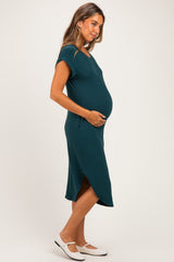 woman wearing a teal maternity dress with short sleeves and a side slit, cradling her baby bump
