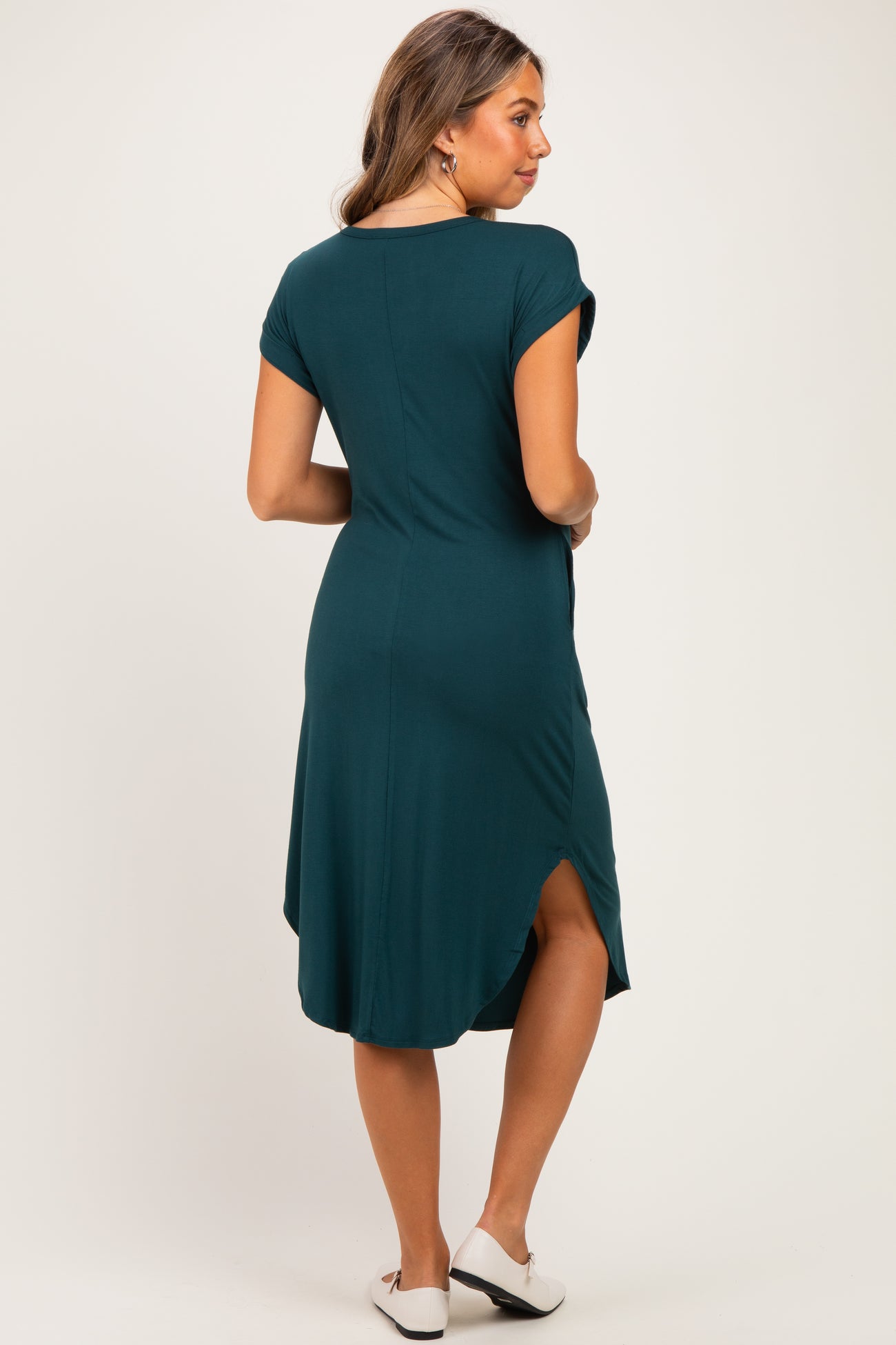 woman wearing a dark teal maternity dress with short sleeves and a curved hem, showing a relaxed fit and a back slit