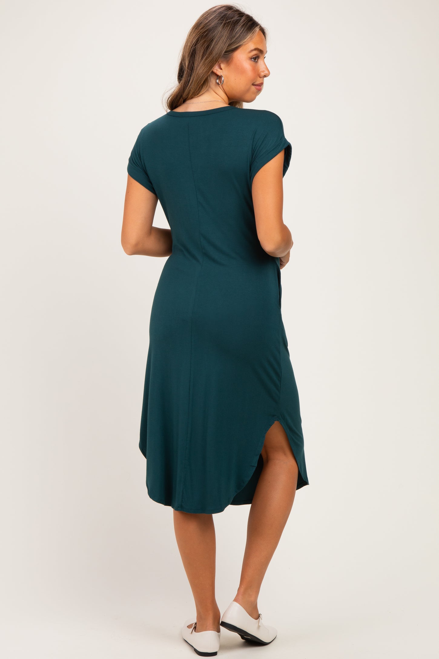 woman wearing a dark teal maternity dress with short sleeves and a curved hem, showing a relaxed fit and a back slit