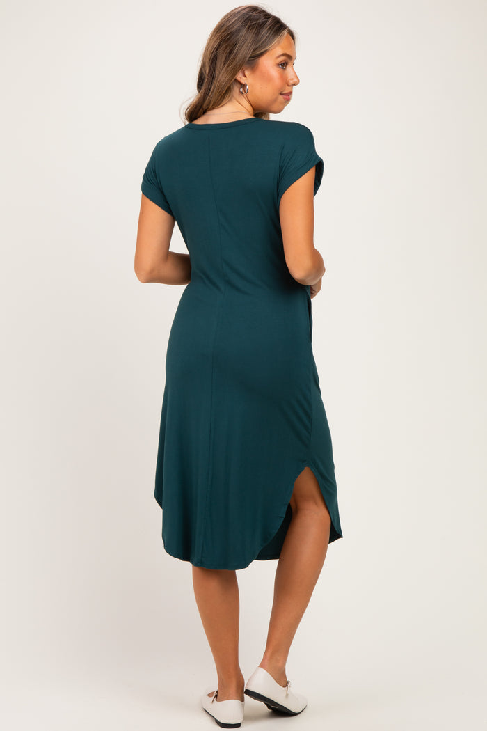 woman wearing a dark teal maternity dress with short sleeves and a curved hem, showing a relaxed fit and a back slit