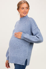 woman wearing a light blue maternity sweater with a high neckline and side slits, holding her baby bump