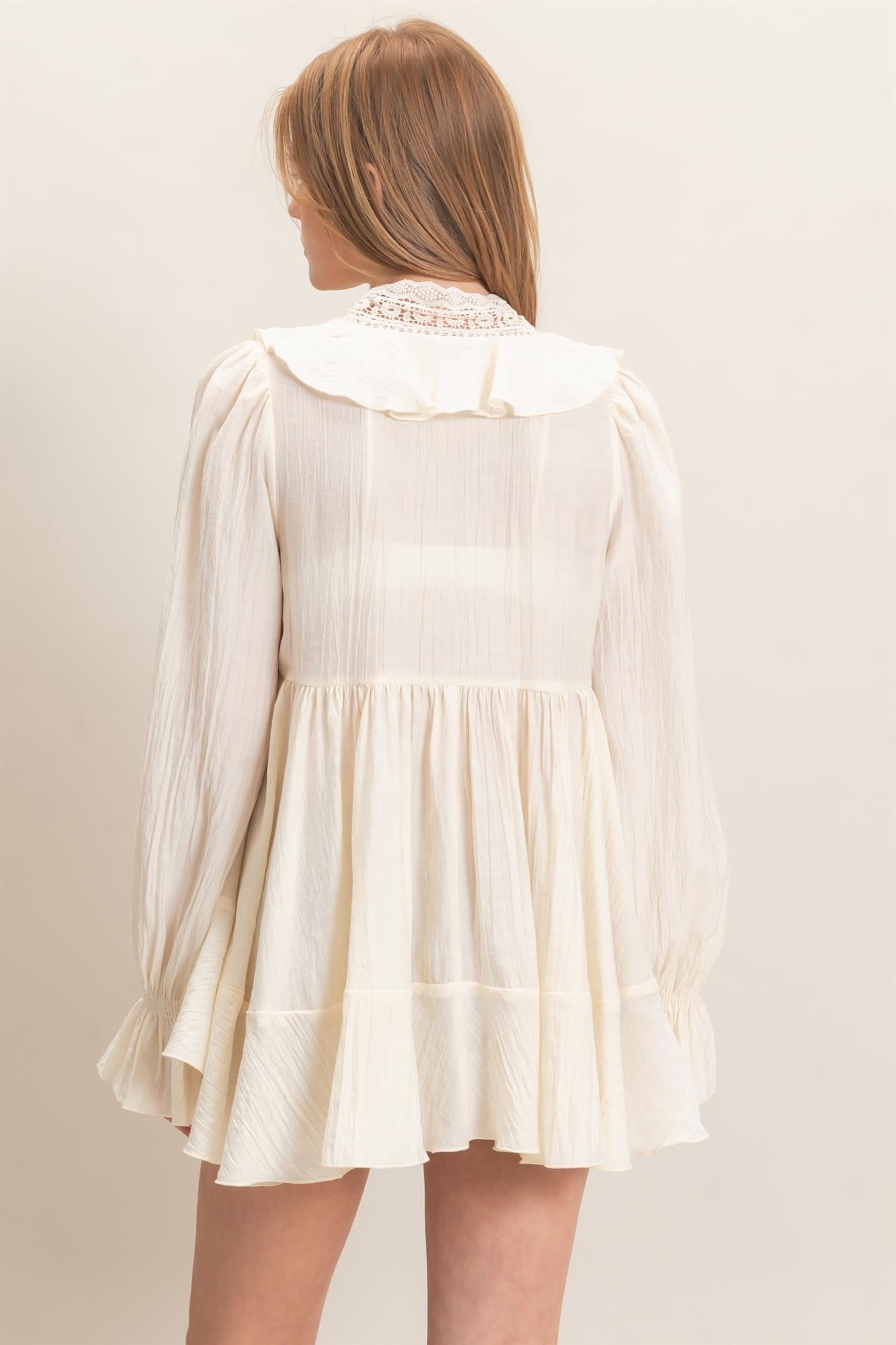 woman wearing a cream-colored long-sleeve dress with a ruffled collar and flared skirt, seen from the back