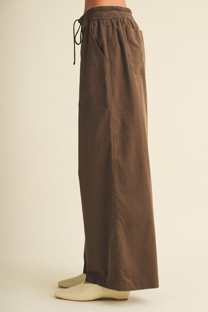 woman wearing brown wide-leg pants with an elastic waistband and pockets, styled with gray socks