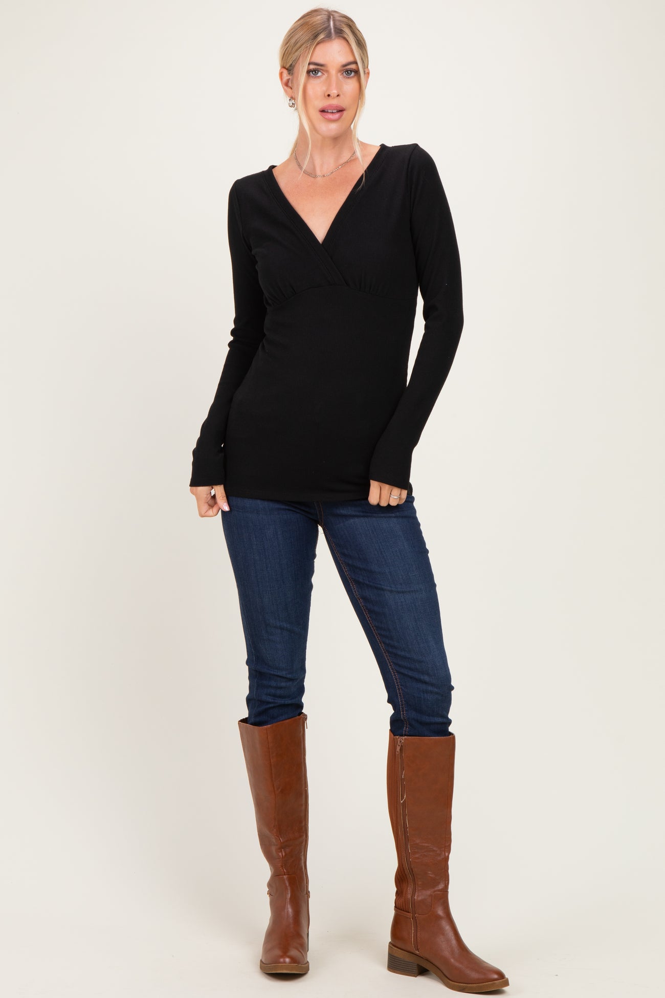 woman wearing a black long sleeve wrap top paired with blue skinny jeans and brown knee-high boots