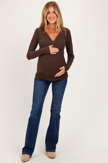 woman wearing a brown long sleeve maternity top and blue jeans, holding her baby bump