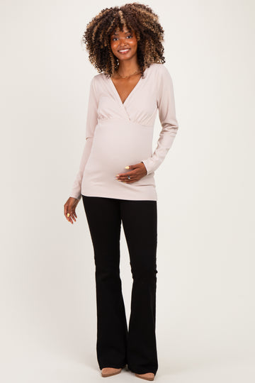 woman wearing a beige long sleeve maternity top with a v-neck and black flared pants, showing her baby bump