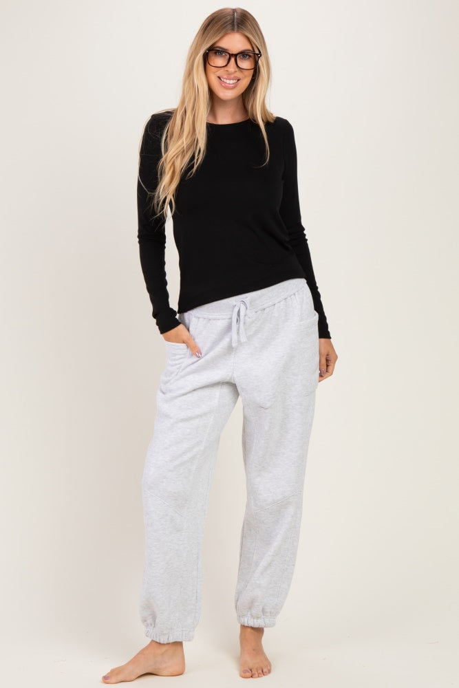 woman wearing a black long sleeve top and light grey drawstring jogger pants, smiling and standing barefoot