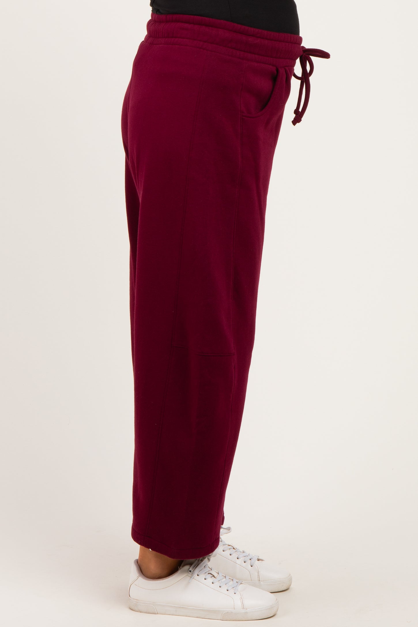 woman wearing burgundy maternity joggers with an elastic waistband and pockets, paired with white sneakers