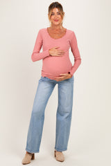 woman wearing a pink long sleeve maternity top with ruffled neckline and blue wide-leg jeans, holding her baby bump