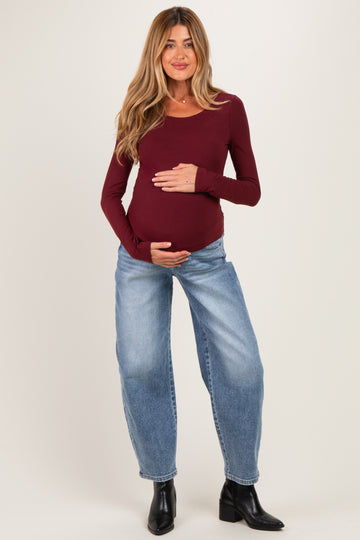 woman wearing a burgundy long sleeve maternity top and holding her baby bump with light blue baggy jeans