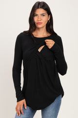 woman wearing a black long sleeve top with a twist detail and a scoop neckline, paired with blue jeans