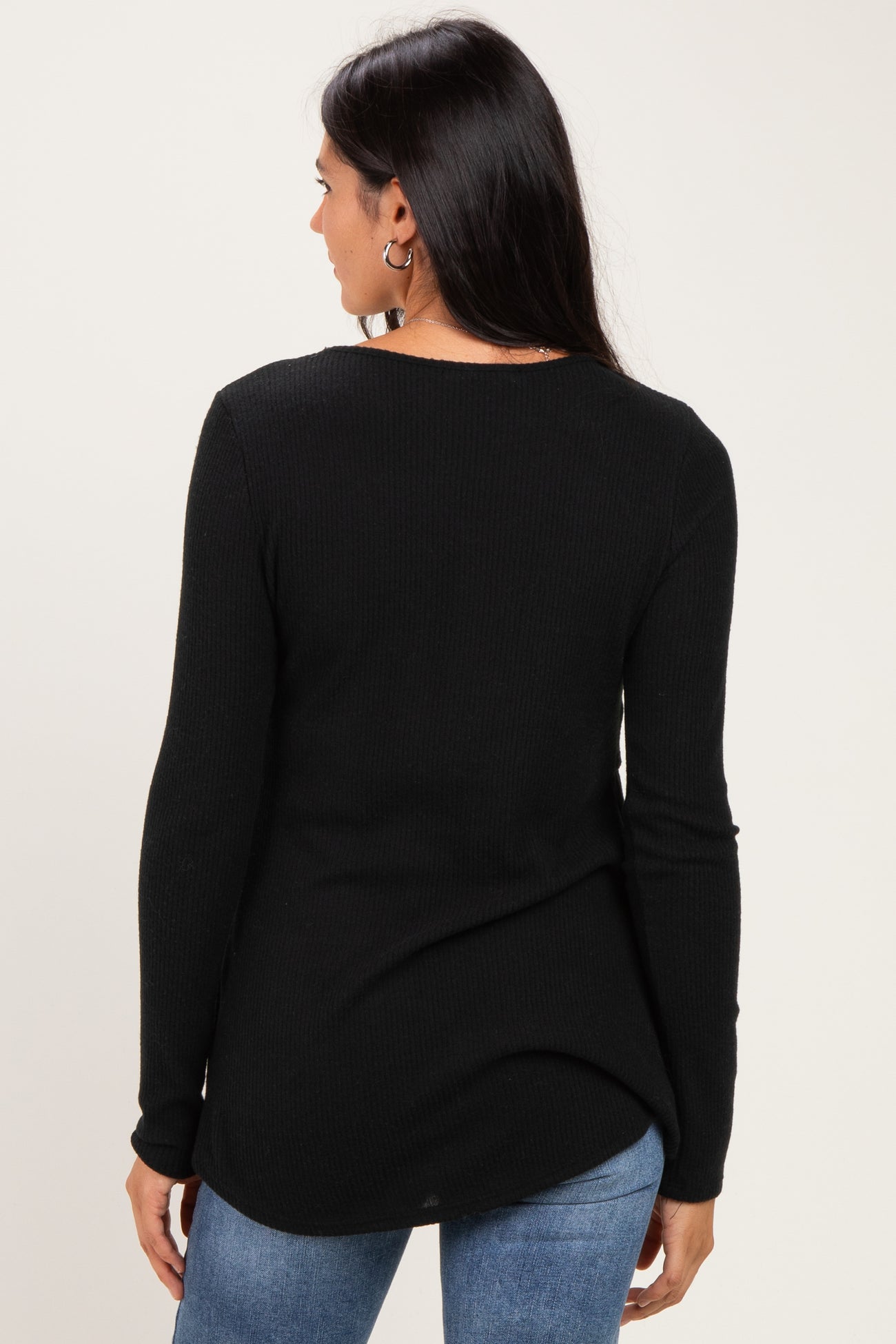 woman wearing a black long sleeve ribbed top with a rounded hem and a relaxed fit, viewed from the back