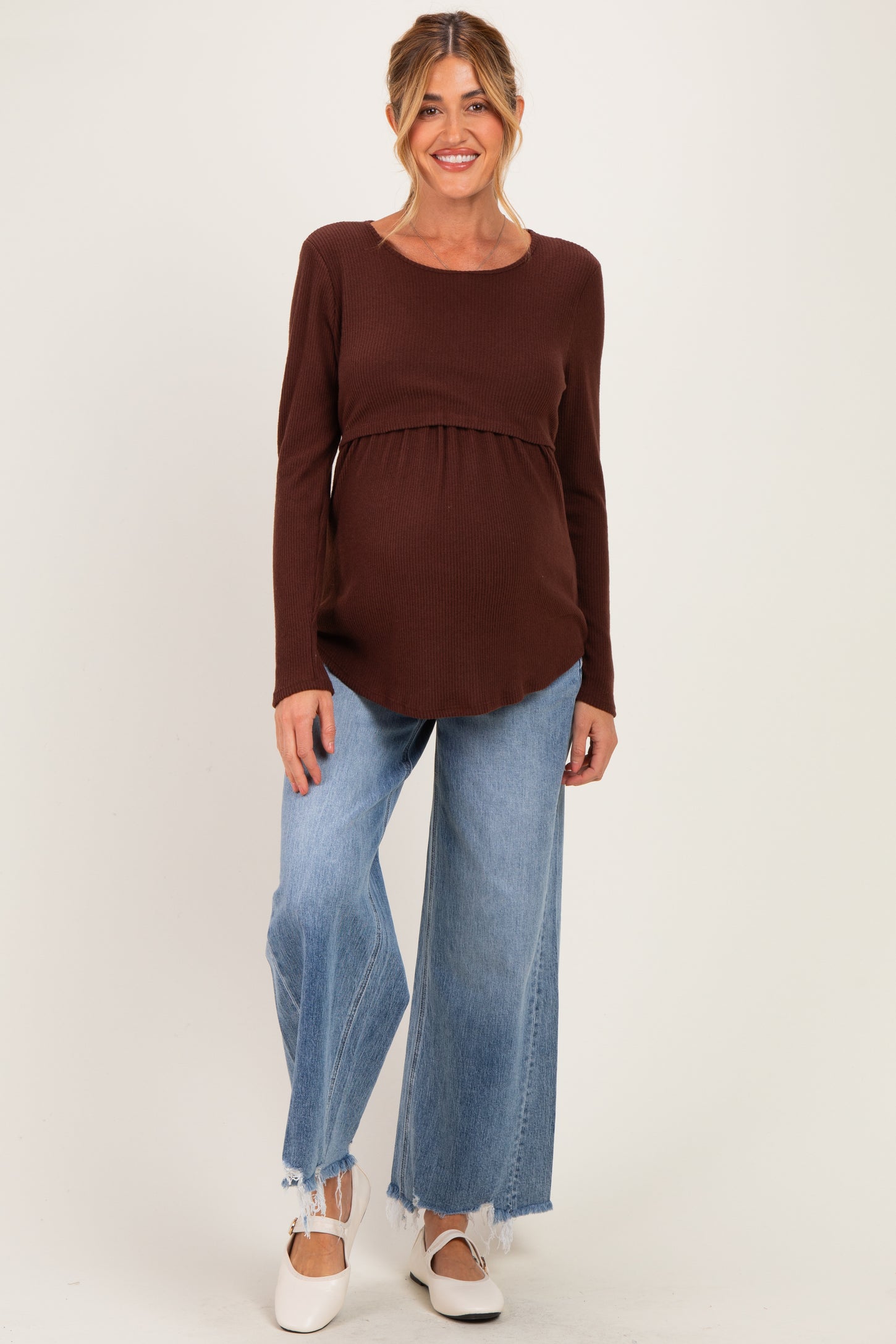 woman wearing a brown maternity long sleeve top and wide leg jeans, showing her baby bump
