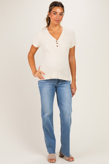 woman wearing a cream ribbed maternity top with short sleeves and button details, showing her baby bump and paired with light blue jeans