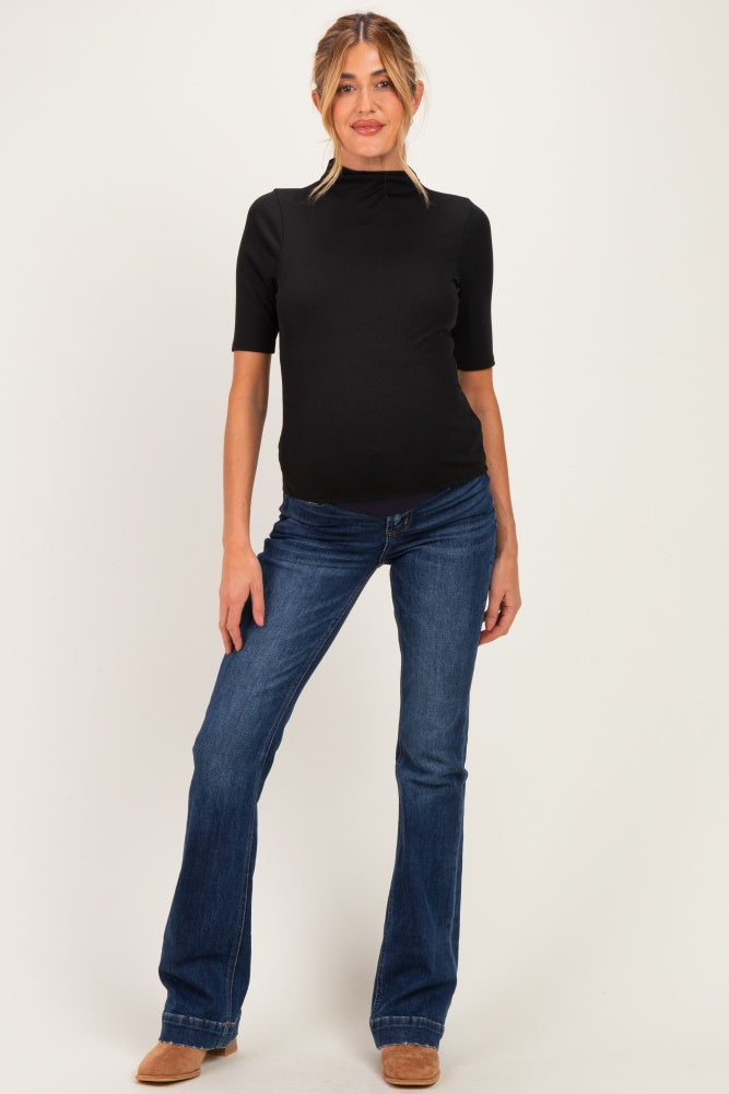 woman wearing a black short sleeve maternity top with a noticeable baby bump and blue flared jeans