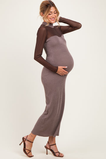 woman wearing a brown ribbed maternity dress with a sheer overlay, gently holding her baby bump