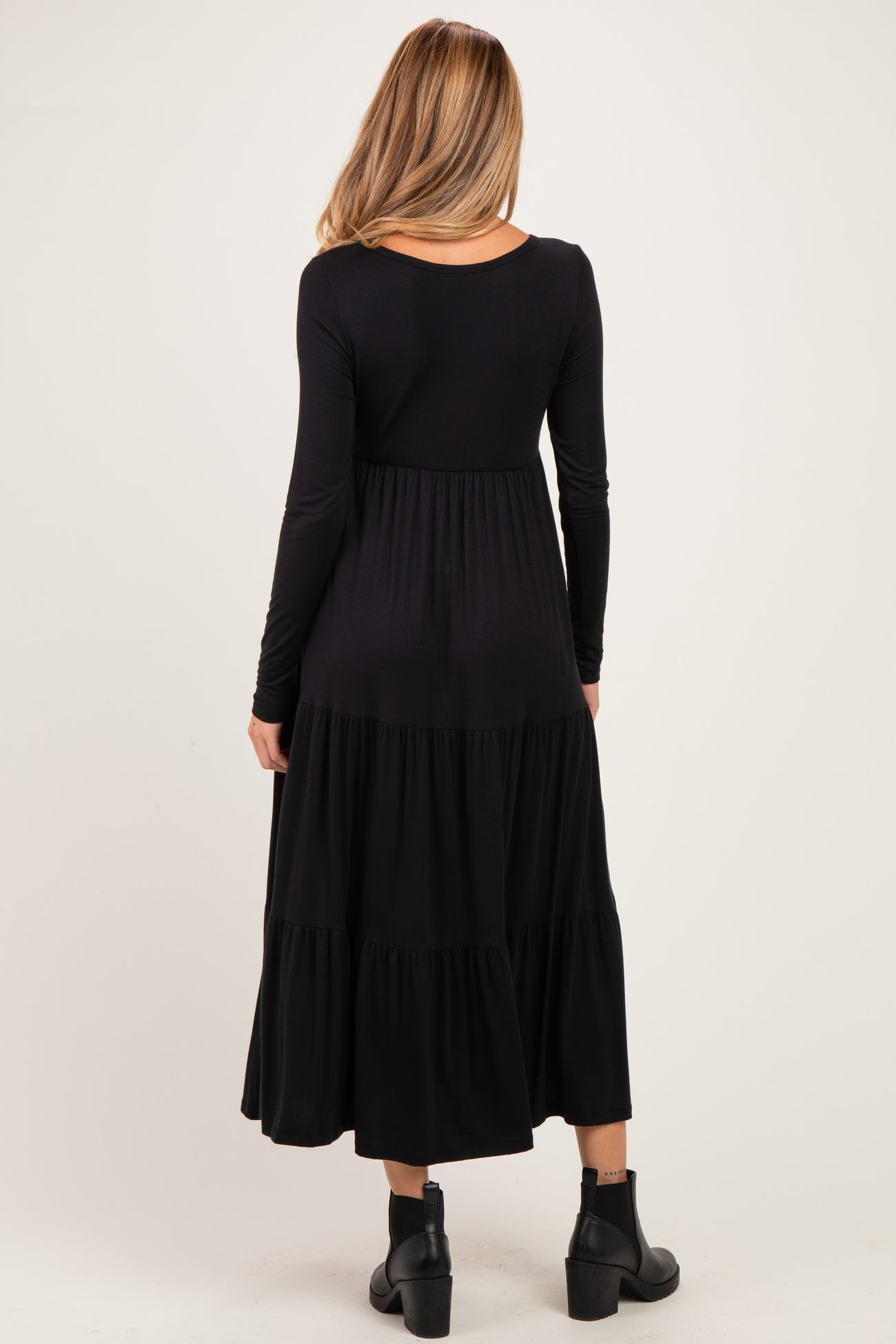 woman wearing a black long sleeve maternity dress with a tiered skirt and a relaxed fit, standing with her back to the camera