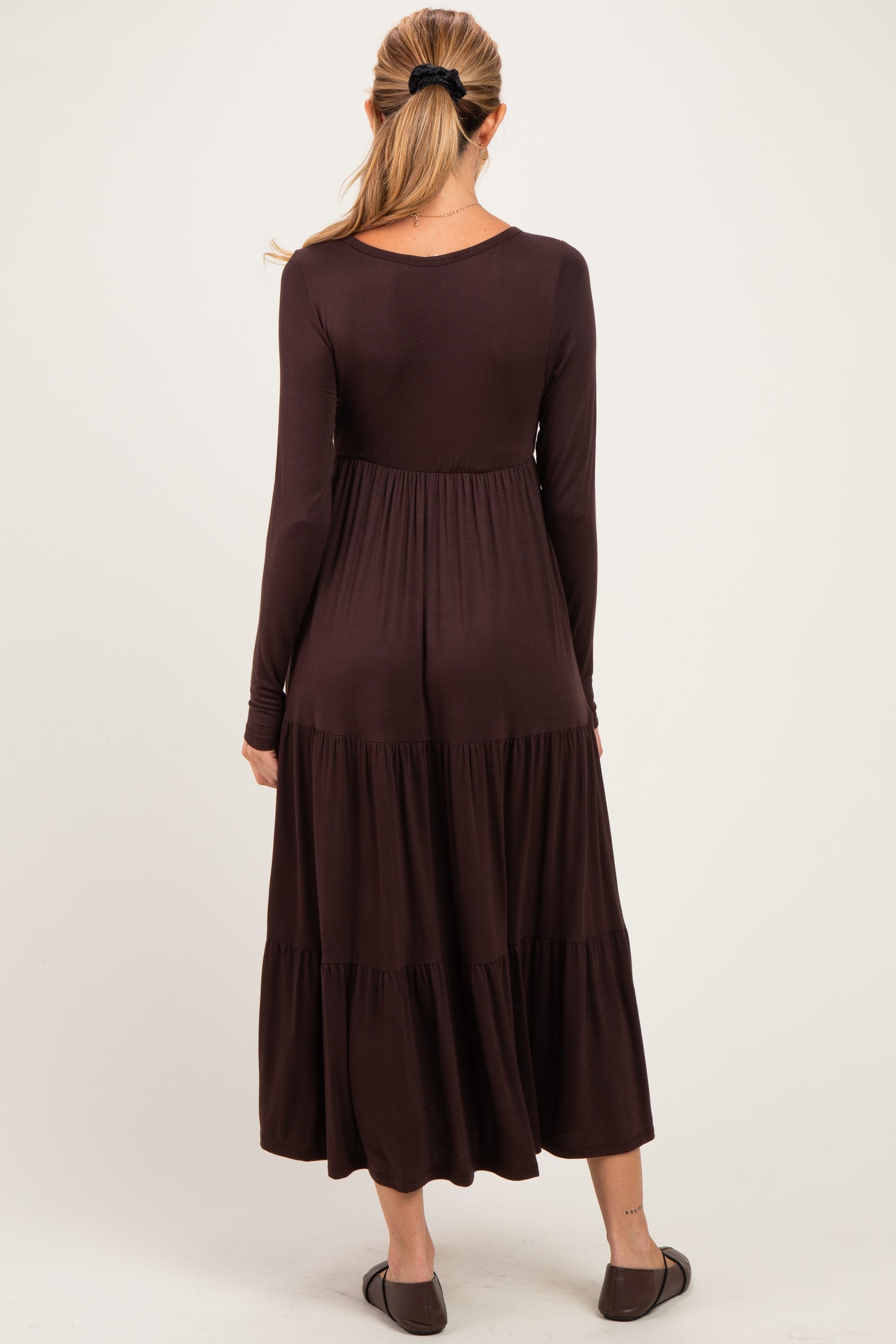 woman wearing a long sleeve dark brown maternity dress with a tiered skirt and a fitted bodice, showing her baby bump