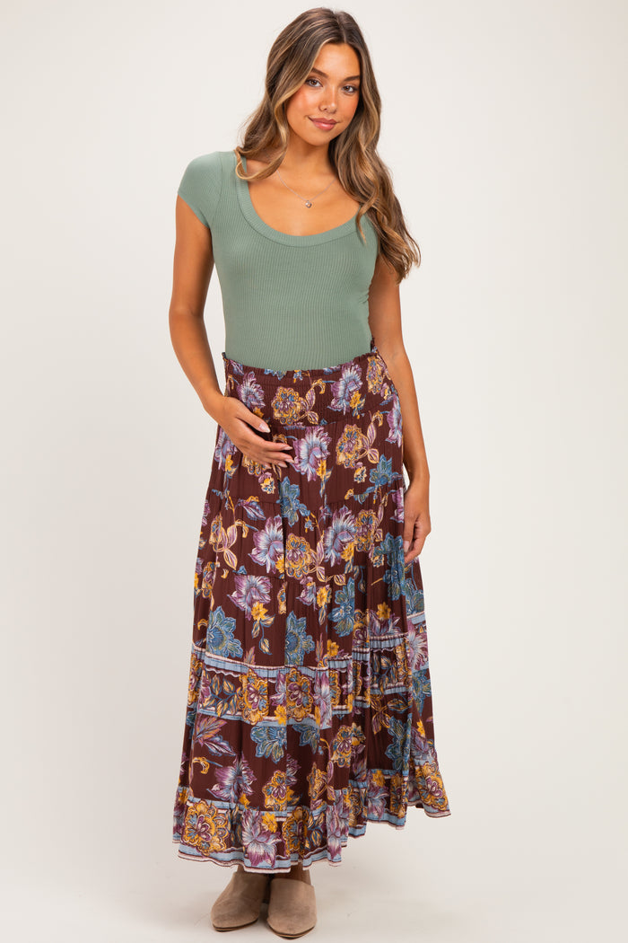 woman wearing a green ribbed maternity top and a long floral maternity maxi skirt, holding her baby bump