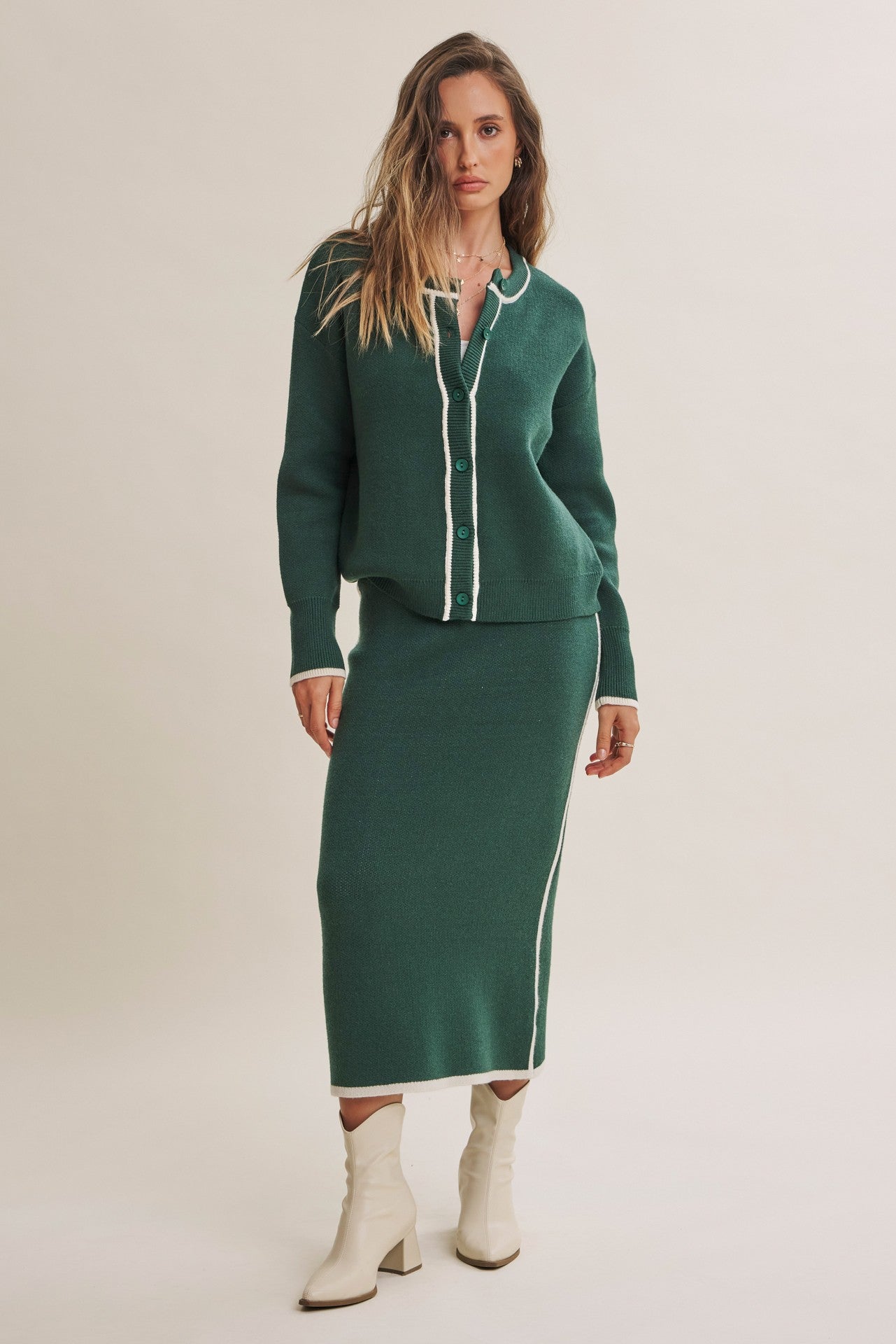 woman wearing a dark green cardigan and matching skirt with white trim and heeled boots