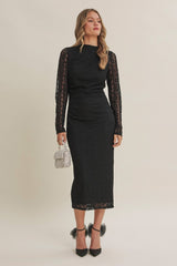 woman wearing a black long sleeve lace midi dress with a fitted silhouette and holding a small purse