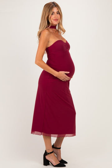 woman wearing a burgundy maternity dress with a fitted bodice and flowing skirt, showing her baby bump