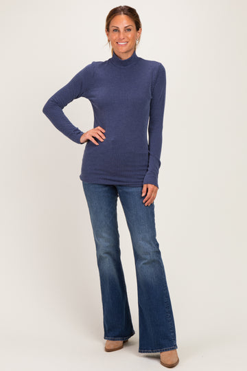 woman wearing a navy ribbed turtleneck sweater and flared jeans, standing with one hand on her hip
