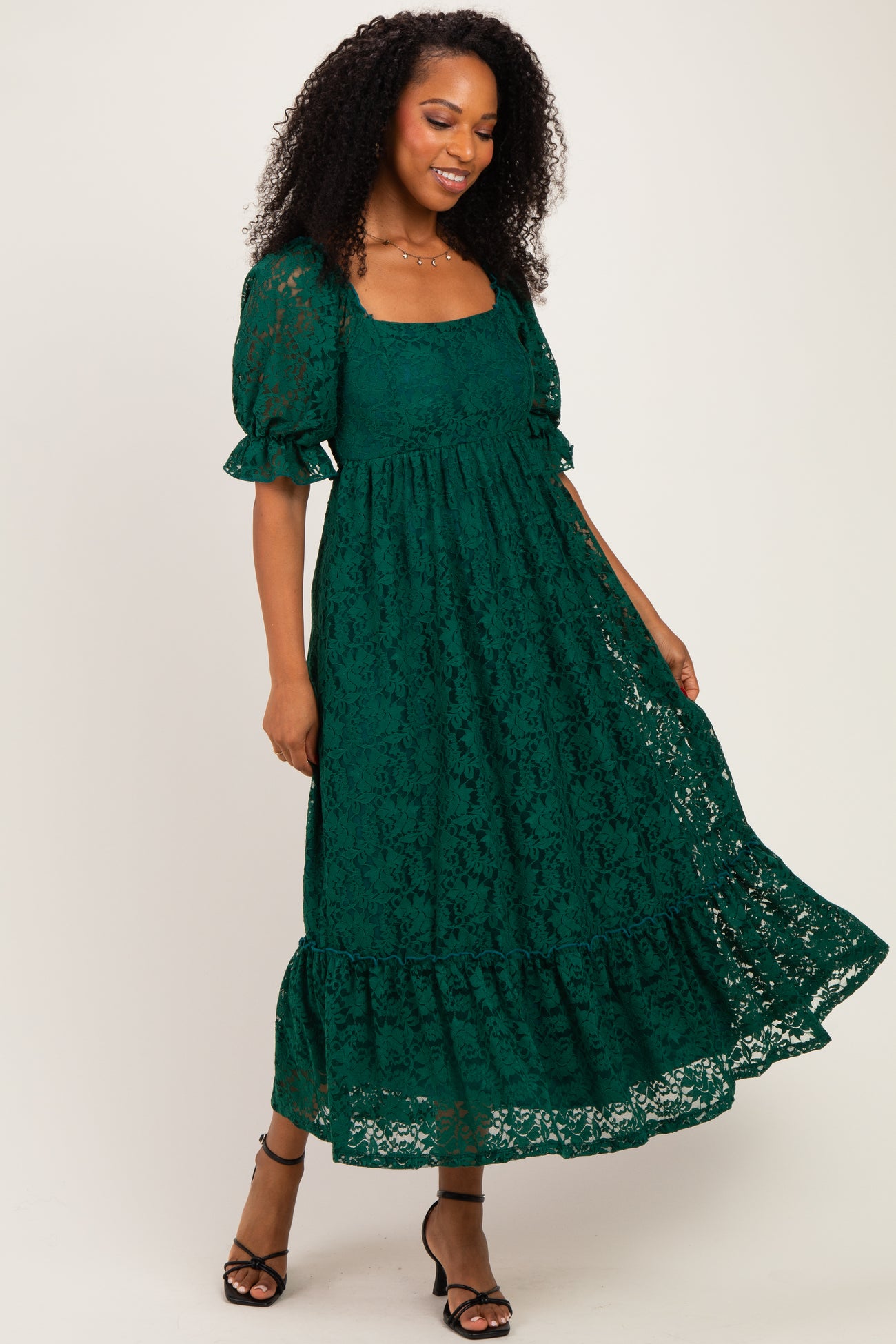 woman wearing a green lace maxi dress with puff sleeves and a tiered hem, posing against a neutral background