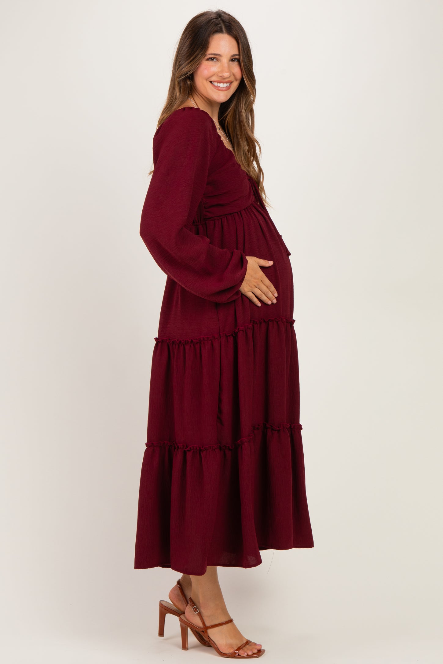 woman wearing a burgundy long sleeve maternity dress with tiered ruffles and a visible baby bump