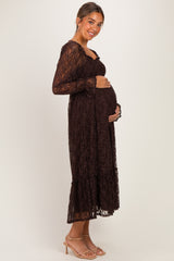 woman wearing a brown lace maternity dress with long sleeves and a tiered skirt, gently holding her baby bump