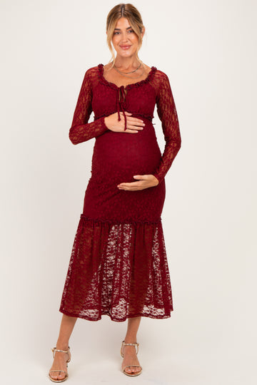 woman wearing a burgundy lace maternity dress with long sleeves and a tiered skirt, cradling her baby bump