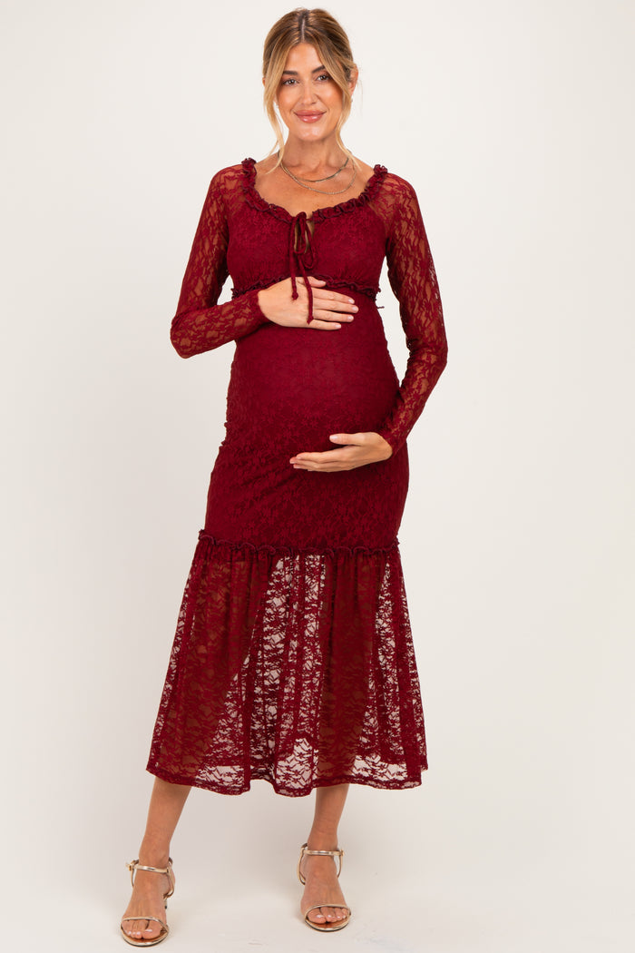 woman wearing a burgundy lace maternity dress with long sleeves and a tiered skirt, cradling her baby bump