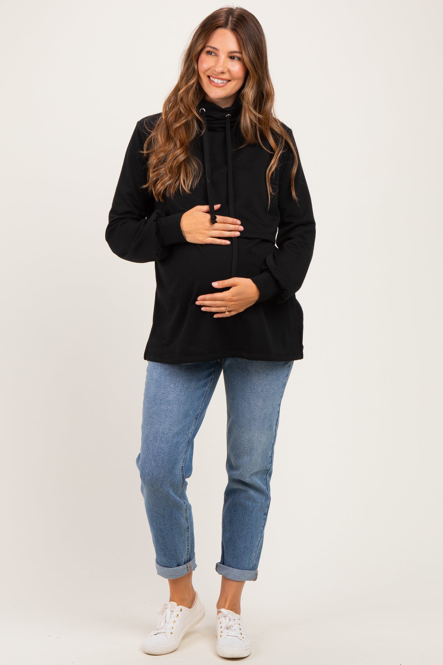 woman wearing a black maternity hoodie and blue jeans, holding her baby bump